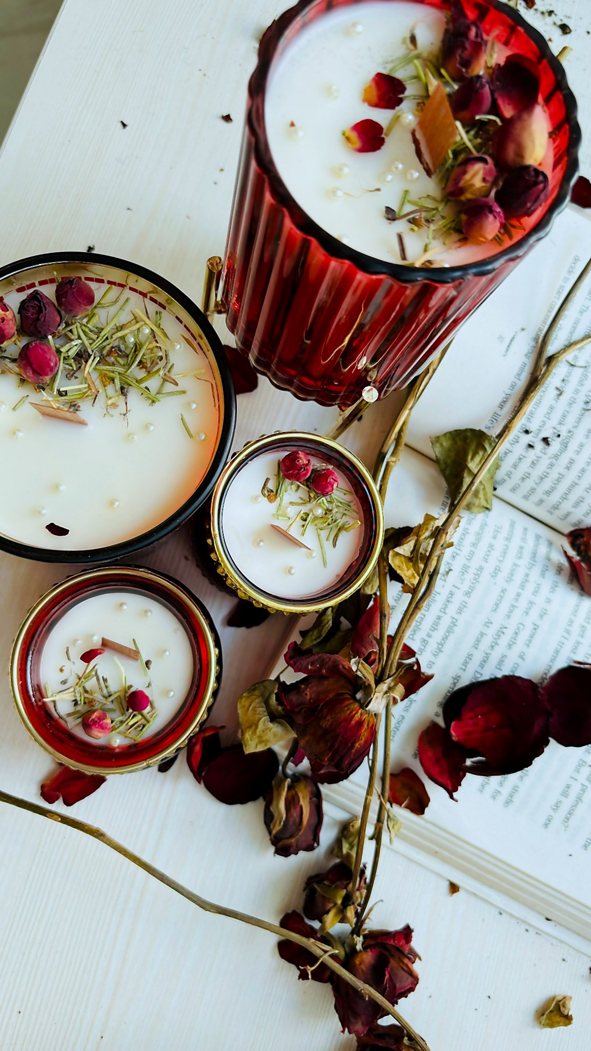 Ruby-red glass vessel candle with dried rose buds on a printed page of poetry
