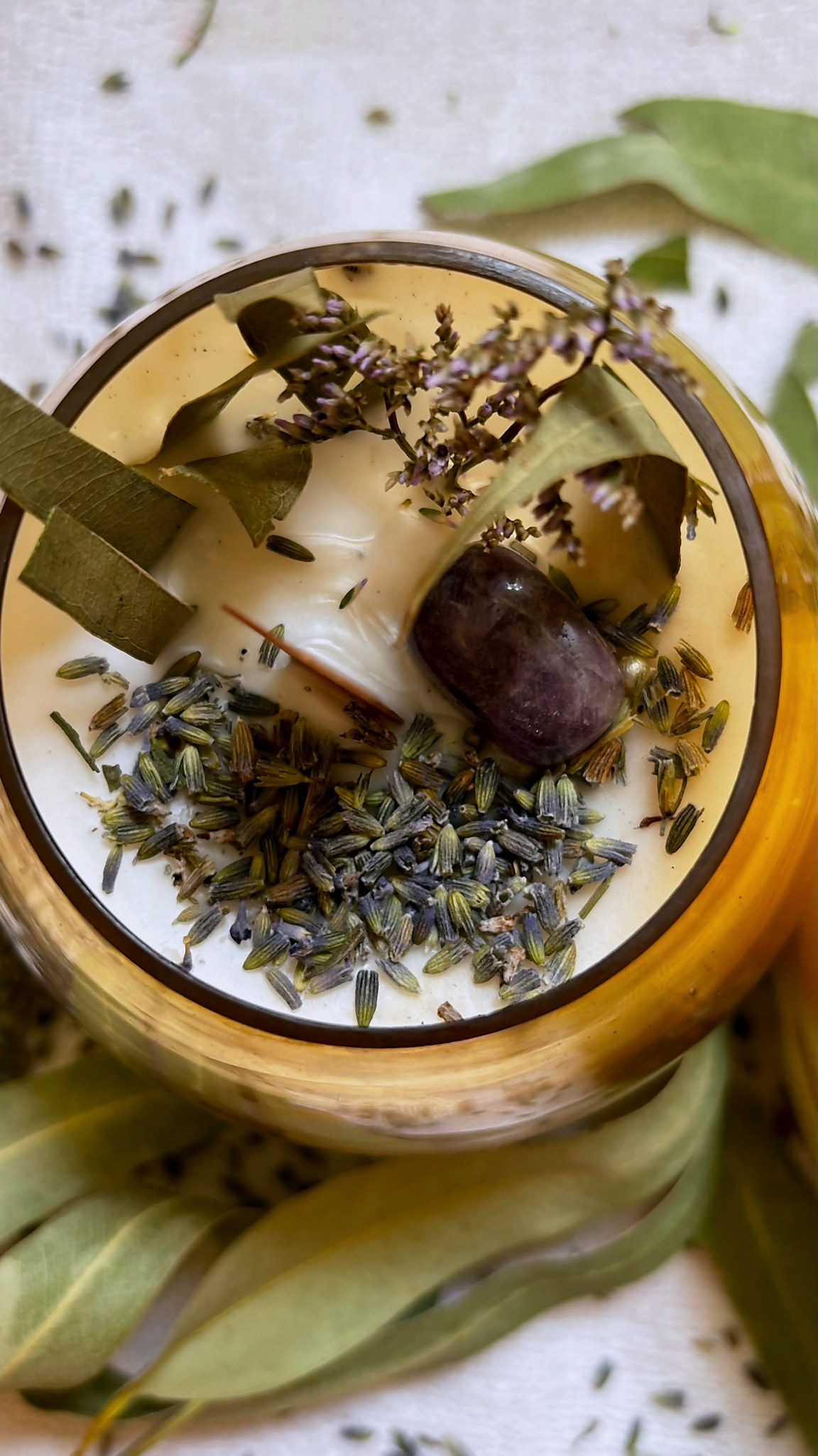 Top-down view of a candle with lavender buds, fennel seeds, bay leaves, and an amethyst crystal set into the wax