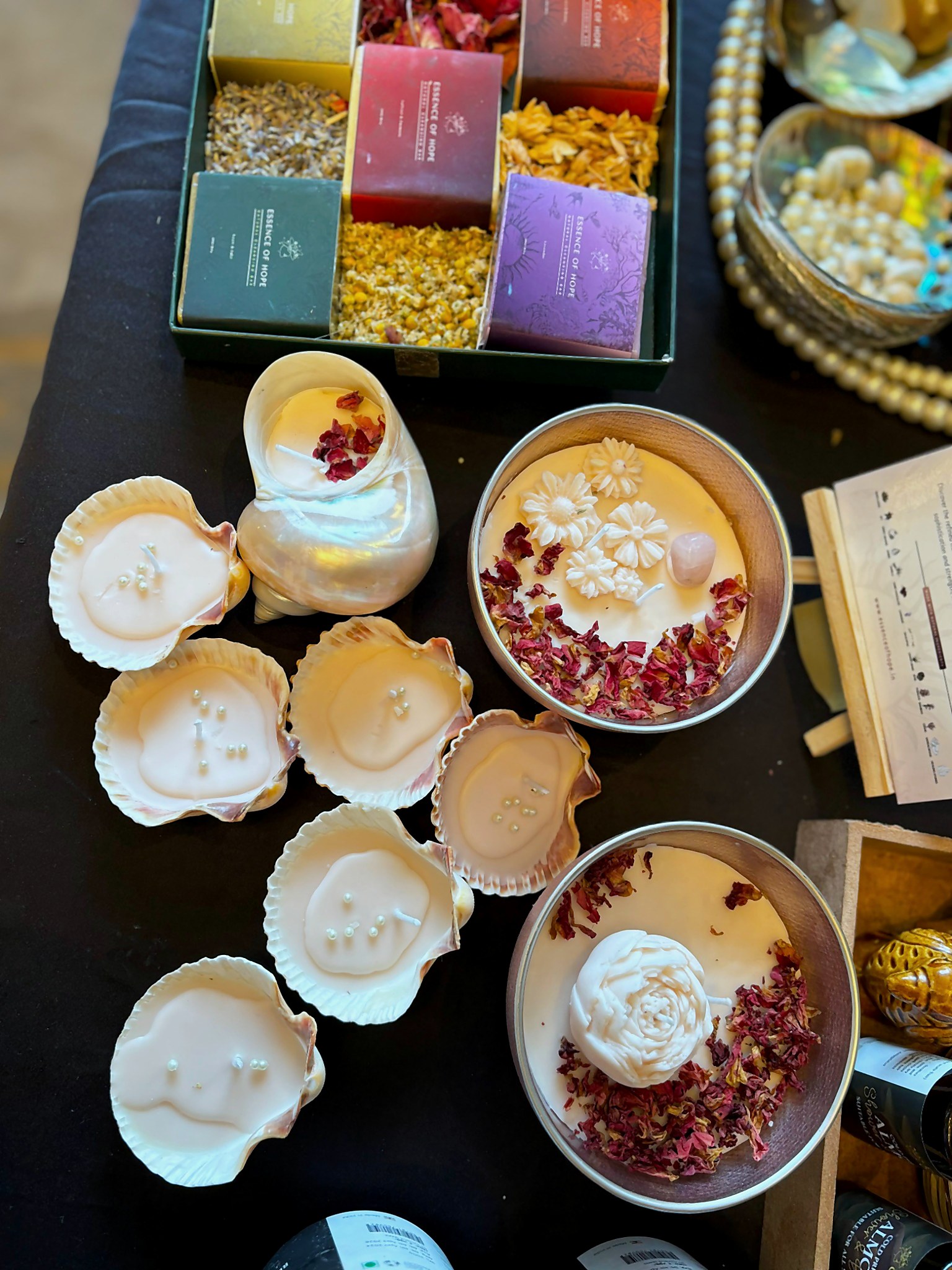 The candles arranged on a dark table with the EOH collection box, copper vessels, dried petals